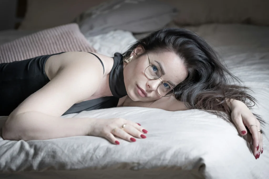 Black-haired beauty with glasses lying on the bed-Electro Sex